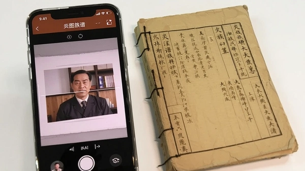 老族谱照片翻拍上传界面,手机屏幕显示炎图族谱app的拍照扫描功能,旁边放着一本泛黄的纸质族谱